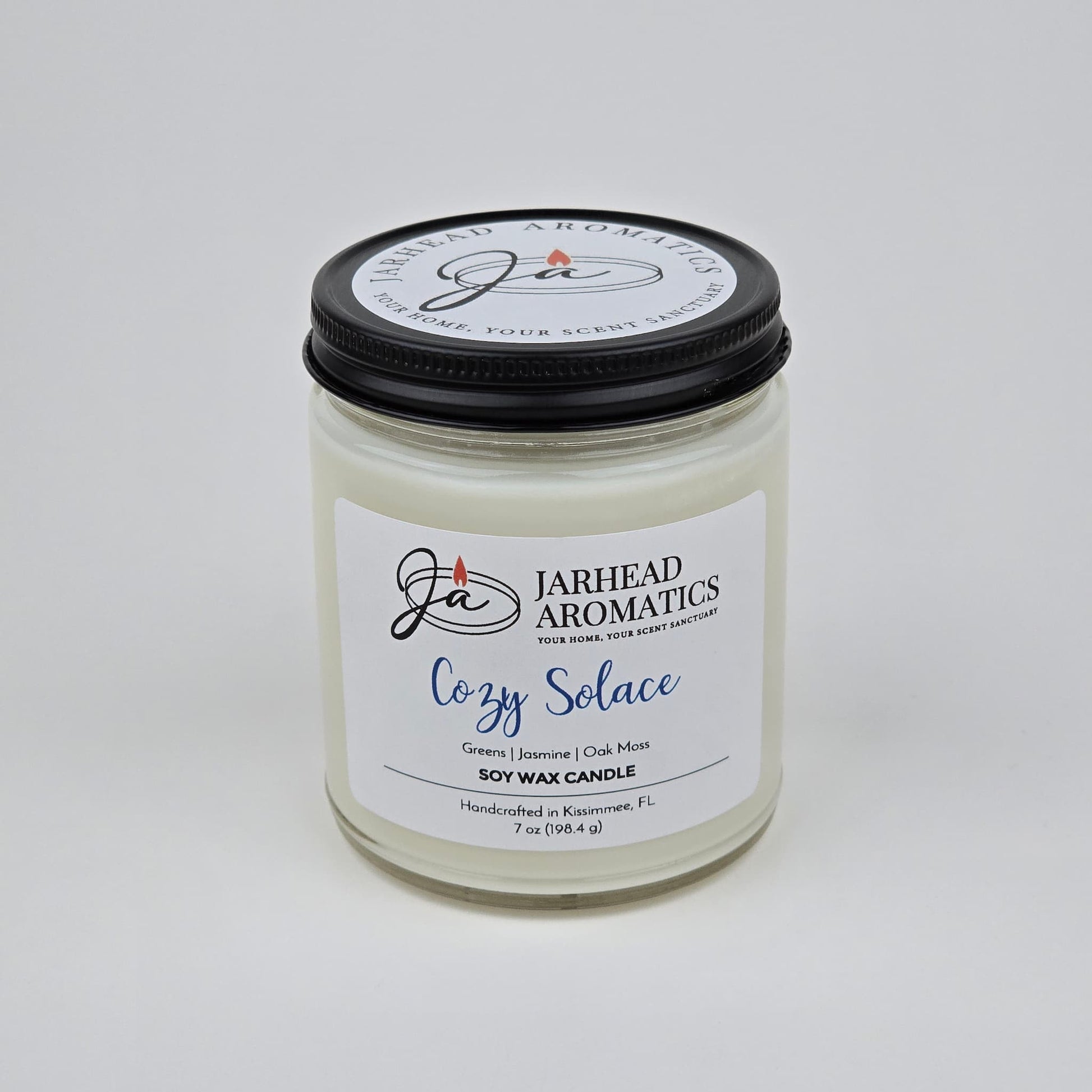 The Cozy Solace Soy Wax Candle by Jarhead Aromatics features fresh greens, jasmine, oak moss, and musk—an ideal fall scent—and comes hand-poured in a clear glass jar with a black lid.