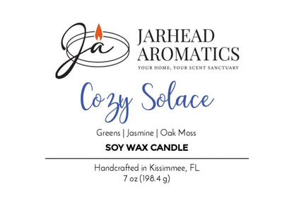 Jarhead Aromatics Cozy Solace Soy Wax Candle label. Showcases scent notes of fresh greens, jasmine, oak moss, and musk for a warm, inviting fall fragrance. Handcrafted in Kissimmee, FL. Features the Jarhead Aromatics logo with a flame above "Ja." 7 oz (198.4g).