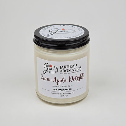A Jarhead Aromatics Cran-Apple Delight Soy Wax Candle, featuring the scent of cranberry, apple, and cinnamon for a long-lasting fragrance, is displayed in a clear jar with a black lid against a plain white background.