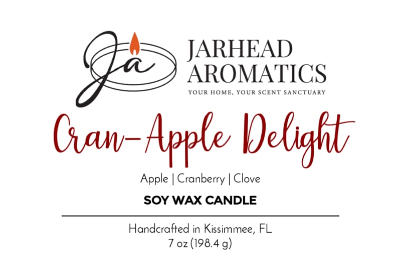 Jarhead Aromatics Cran-Apple Delight Soy Wax Candle features a delightful blend of cranberry, apple, and cinnamon scents. This 7 oz candle is handcrafted in Kissimmee, FL for a long-lasting fragrance experience. The label showcases black and red text alongside a flame graphic.