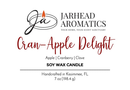Jarhead Aromatics Cran-Apple Delight Soy Wax Candle features a delightful blend of cranberry, apple, and cinnamon scents. This 7 oz candle is handcrafted in Kissimmee, FL for a long-lasting fragrance experience. The label showcases black and red text alongside a flame graphic.