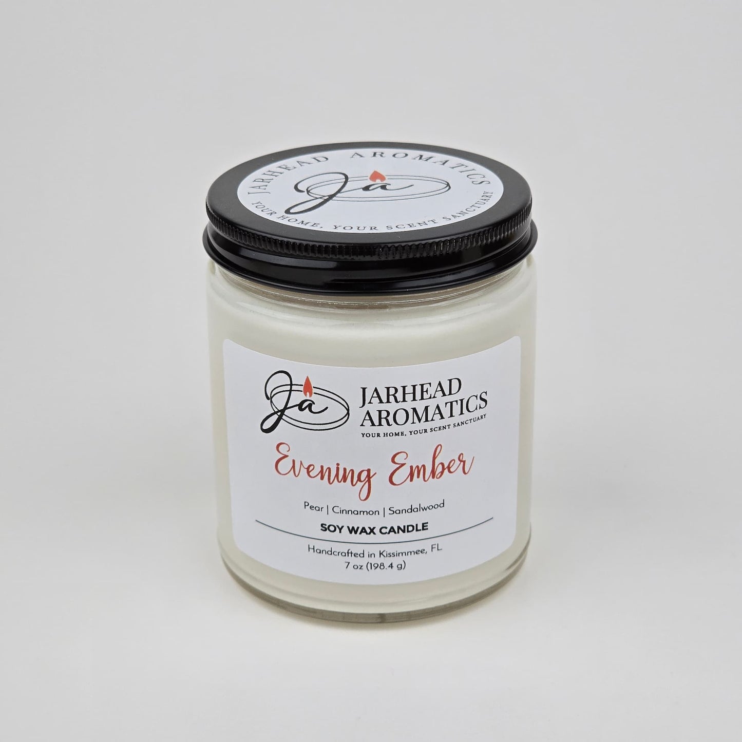 A white premium soy wax candle from Jarhead Aromatics, labeled Evening Ember Soy Wax Candle | Plum, Sandalwood & Smoke Candle, housed in a glass jar with a sleek black lid. This handcrafted candle is made in Kissimmee, FL and features notes of plum, sandalwood, and smoke.