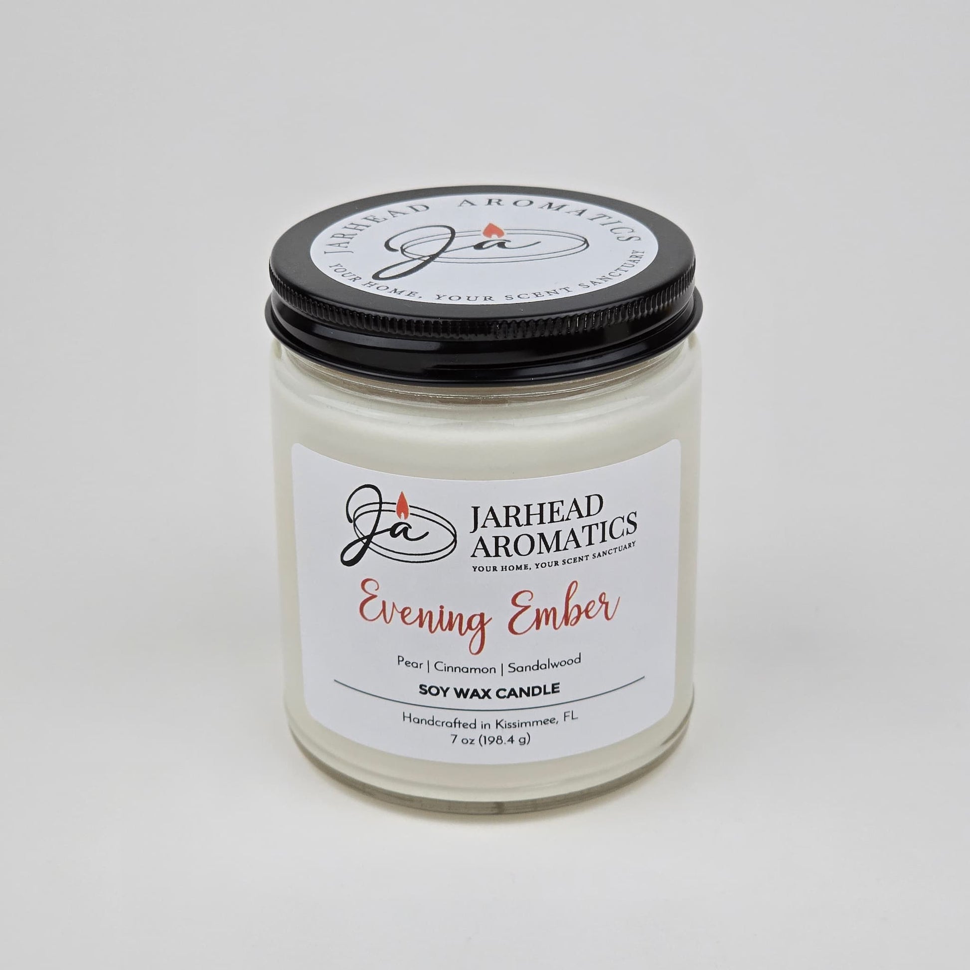 A white premium soy wax candle from Jarhead Aromatics, labeled Evening Ember Soy Wax Candle | Plum, Sandalwood & Smoke Candle, housed in a glass jar with a sleek black lid. This handcrafted candle is made in Kissimmee, FL and features notes of plum, sandalwood, and smoke.