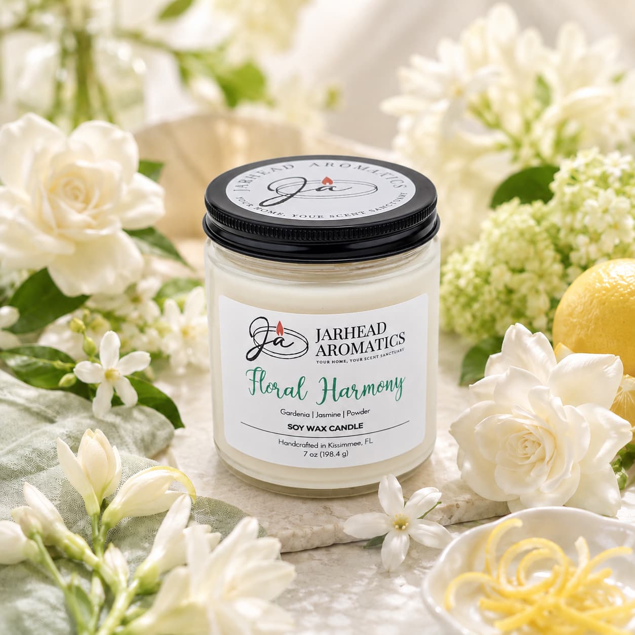 The Jarhead Aromatics Floral Harmony Soy Wax Candle, featuring notes of gardenia, jasmine, and tuberose, is displayed amidst white blossoms, green foliage, and lemon zest on a light surface for a fresh and sophisticated ambiance. This hand-poured candle enhances your space with its elegant design while providing long-lasting floral fragrance to be enjoyed for hours.