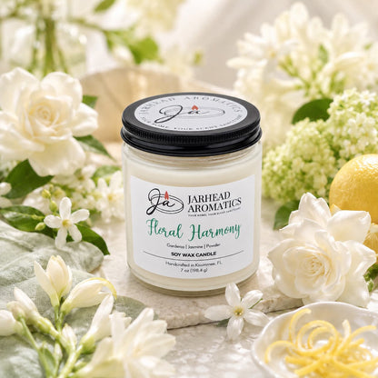 The Jarhead Aromatics Floral Harmony Soy Wax Candle, featuring notes of gardenia, jasmine, and tuberose, is displayed amidst white blossoms, green foliage, and lemon zest on a light surface for a fresh and sophisticated ambiance. This hand-poured candle enhances your space with its elegant design while providing long-lasting floral fragrance to be enjoyed for hours.
