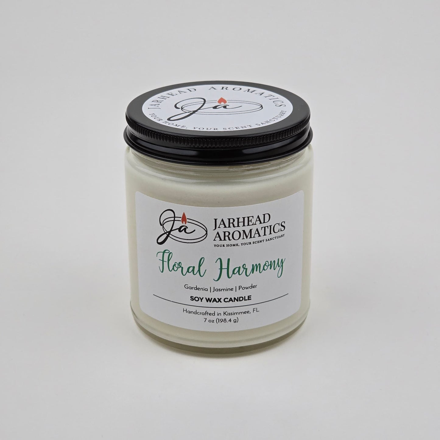 Experience the Floral Harmony Soy Wax Candle by Jarhead Aromatics—a hand-poured candle crafted in Kissimmee, FL. Presented in a clear jar with a black lid featuring the brand logo and text, this candle blends gardenia, jasmine, and tuberose for a long-lasting fragrance that infuses your space with delicate white floral notes.