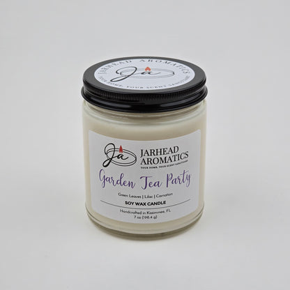 A white soy wax candle in a clear glass jar with a black lid. The label reads Jarhead Aromatics Garden Tea Party Soy Wax Candle | Rose, Jasmine & Green Floral Candle. This handcrafted floral scented candle, featuring notes of rose, jasmine, and green florals, is made by Jarhead Aromatics in Kissimmee, FL.