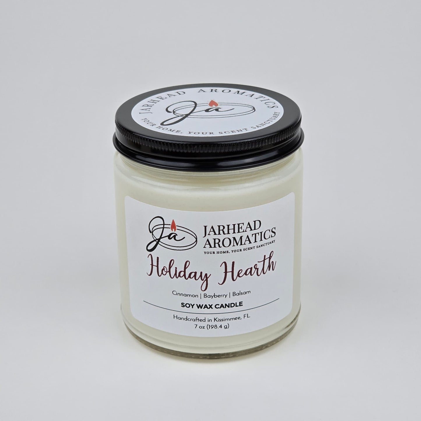The Jarhead Aromatics Holiday Hearth Soy Wax Candle features festive notes of cinnamon clove, bayberry, and balsam to fill your home with holiday warmth. This 7 oz white candle comes in a glass jar with a black lid, making it the perfect addition for seasonal ambiance in any room.