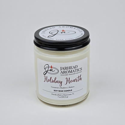 The Jarhead Aromatics Holiday Hearth Soy Wax Candle features festive notes of cinnamon clove, bayberry, and balsam to fill your home with holiday warmth. This 7 oz white candle comes in a glass jar with a black lid, making it the perfect addition for seasonal ambiance in any room.
