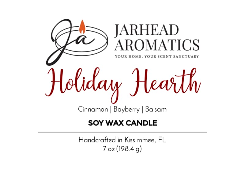 Jarhead Aromatics Holiday Hearth Soy Wax Candle | Cinnamon Clove, Bayberry & Balsam Holiday Candle label. This handcrafted scented soy candle, made in Kissimmee, FL, combines the festive aromas of cinnamon clove, bayberry, and balsam to create a warm holiday ambiance. Net weight 7 oz (198.4g). Features a stylized "Ja" logo with a candle flame.