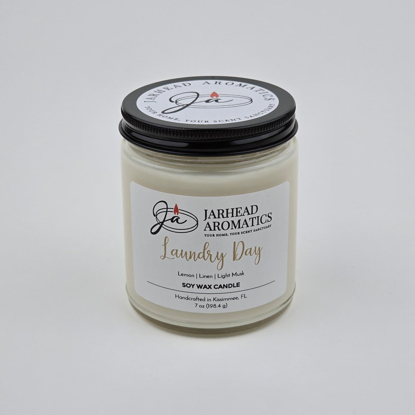 A 7 oz Jarhead Aromatics Laundry Day Soy Wax Candle, featuring fresh linen, lemon, and light musk scents. Handcrafted in Kissimmee, FL for a long-lasting aroma. The candle is displayed against a plain white background.