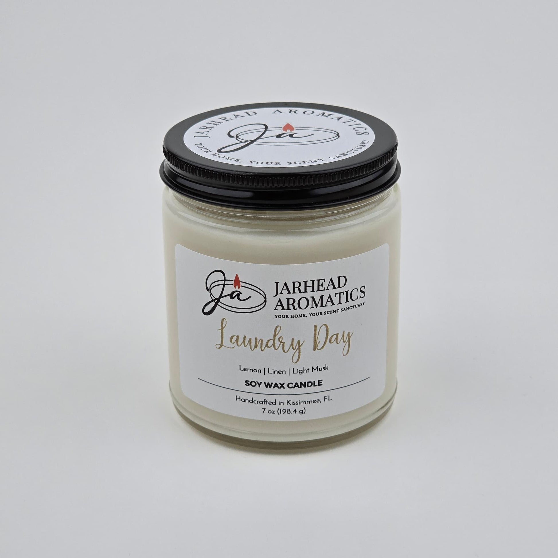 A 7 oz Jarhead Aromatics Laundry Day Soy Wax Candle, featuring fresh linen, lemon, and light musk scents. Handcrafted in Kissimmee, FL for a long-lasting aroma. The candle is displayed against a plain white background.