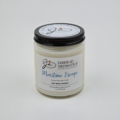 Introducing the Maritime Escape Soy Wax Candle by Jarhead Aromatics—a 7 oz white jar candle with a sleek black lid. Handcrafted in Kissimmee, FL, this coastal-inspired candle features notes of sea salt, ozone, and cedar for a fresh ocean fragrance. Its inviting scent brings refreshing seaside vibes to any space.