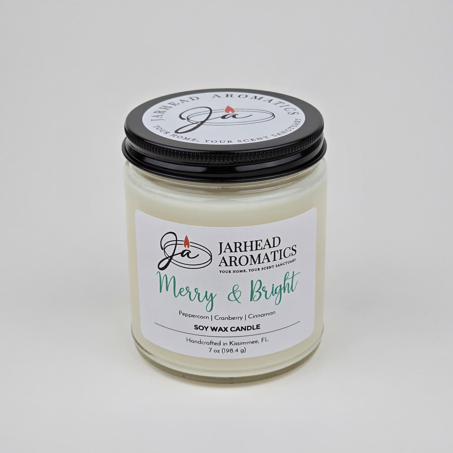 A white Merry & Bright Soy Wax Candle by Jarhead Aromatics with a black lid is displayed against a plain white background. The label reads "Merry & Bright" and features notes of citrus cranberry, warm spice, and fir—capturing the essence of a festive holiday fragrance.