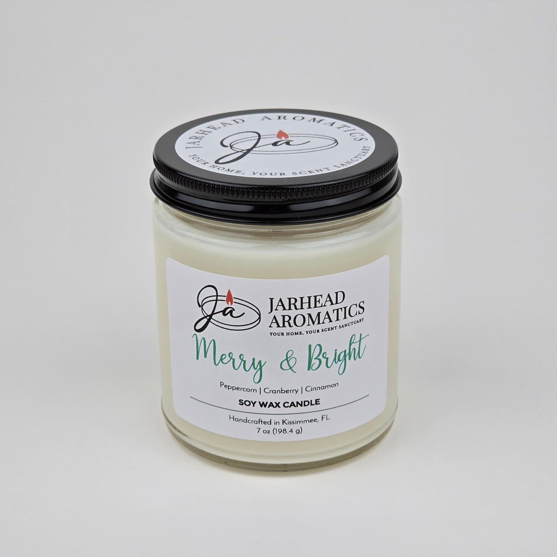 A white Merry & Bright Soy Wax Candle by Jarhead Aromatics with a black lid is displayed against a plain white background. The label reads "Merry & Bright" and features notes of citrus cranberry, warm spice, and fir—capturing the essence of a festive holiday fragrance.