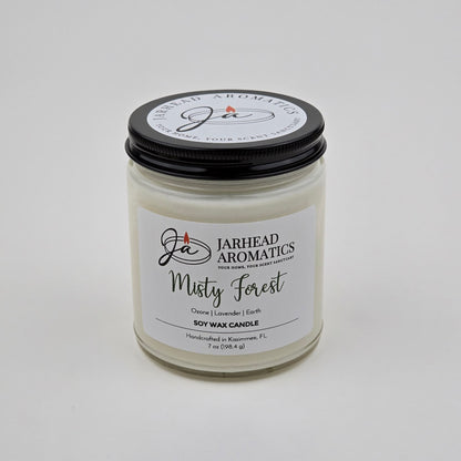 A white natural soy wax candle in a glass jar labeled Jarhead Aromatics Misty Forest Soy Wax Candle, featuring earthy moss, lavender, and juniper scents. This forest-inspired candle includes a black lid and is handcrafted in Kissimmee, FL.