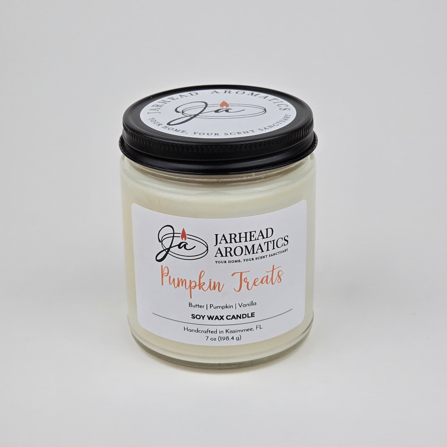 A white jar candle from Jarhead Aromatics, labeled Pumpkin Treats Soy Wax Candle, features a blend of pumpkin caramel, maple pecan, and vanilla fragrances. Handcrafted in Kissimmee, FL and weighing 7 oz, this autumn candle is made from soy wax—perfect for filling your home with a cozy fall scent.