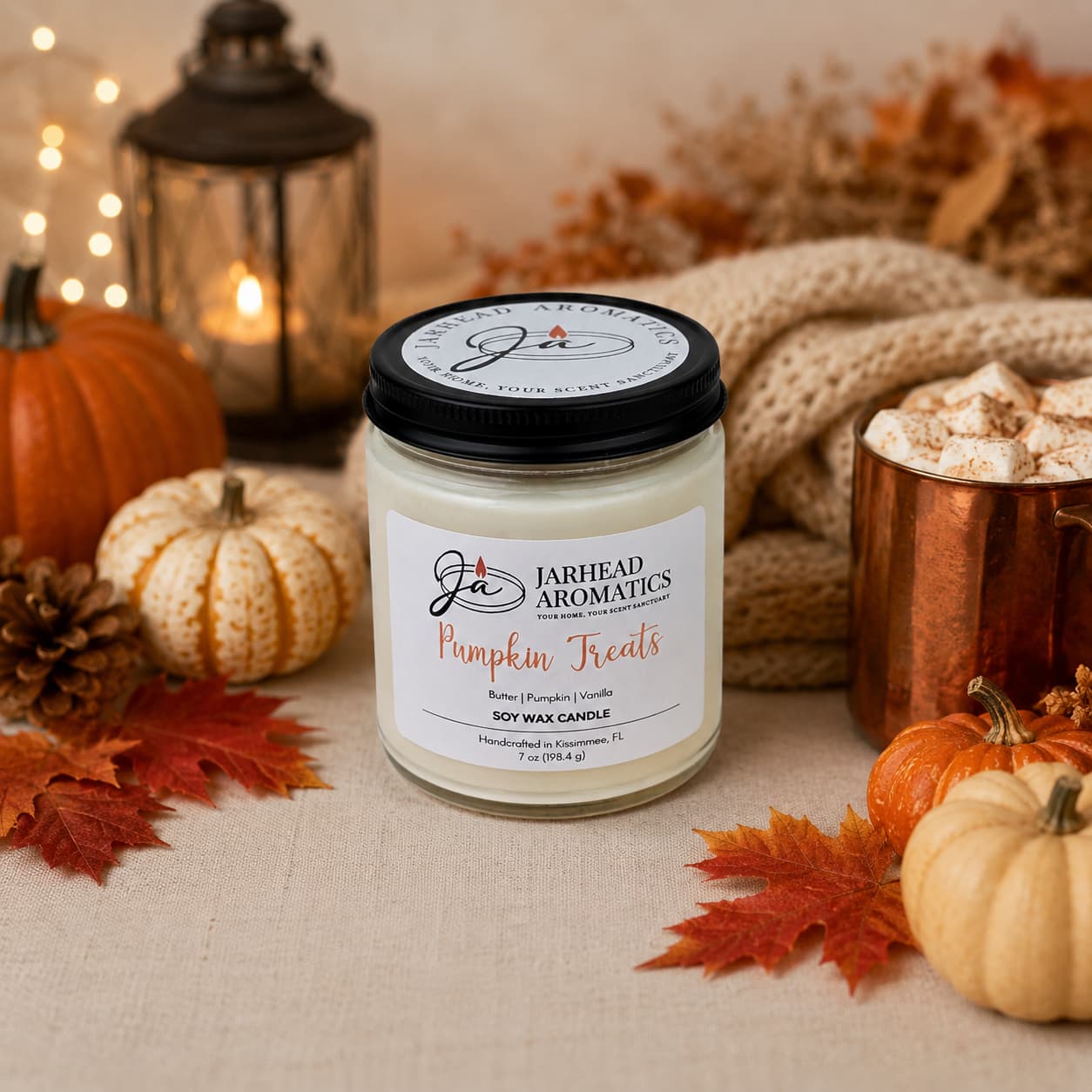 A Jarhead Aromatics Pumpkin Treats Soy Wax Candle, featuring pumpkin caramel, maple pecan, and vanilla notes, sits on a table surrounded by mini pumpkins, fall leaves, a cozy knit blanket, a lantern, and a mug of marshmallows—creating a warm autumn atmosphere filled with inviting fall fragrance.