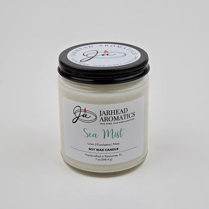 A white glass jar candle labeled Jarhead Aromatics Sea Mist Soy Wax Candle | Clean Coastal Linen & Sea Salt Candle, featuring notes of linen, eucalyptus, and moss. Handcrafted in Kissimmee, FL, this coastal candle offers an aquatic floral fragrance and comes topped with a black lid.