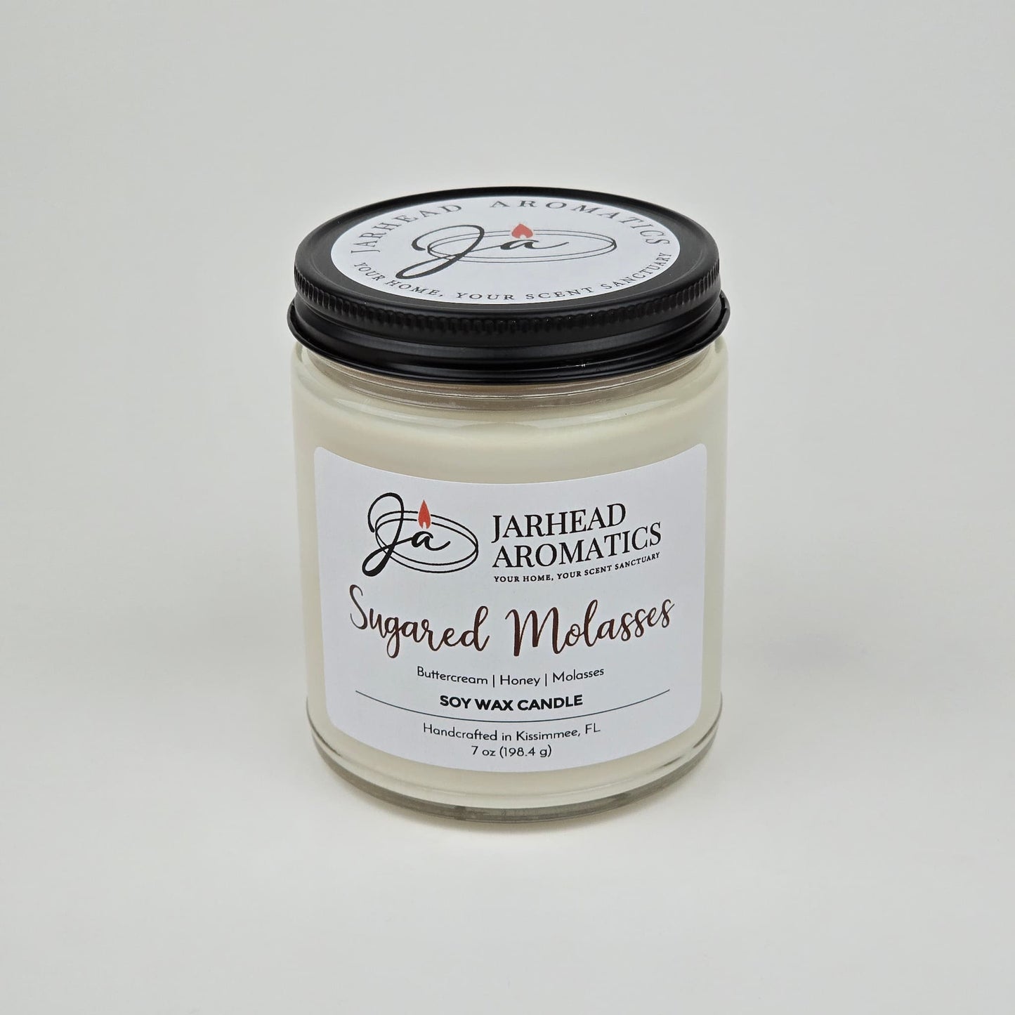 The Jarhead Aromatics Sugared Molasses Soy Wax Candle, labeled as "Sugared Molasses Soy Wax Candle | Brown Sugar, Honey, Cinnamon & Molasses Fall Candle," is a handmade soy candle that combines the warm, rich fragrance of brown sugar, honey, cinnamon, and molasses. Presented in a clear glass jar with a black lid and a crisp white label, this candle offers both an elegant look and an irresistible autumn-inspired aroma.