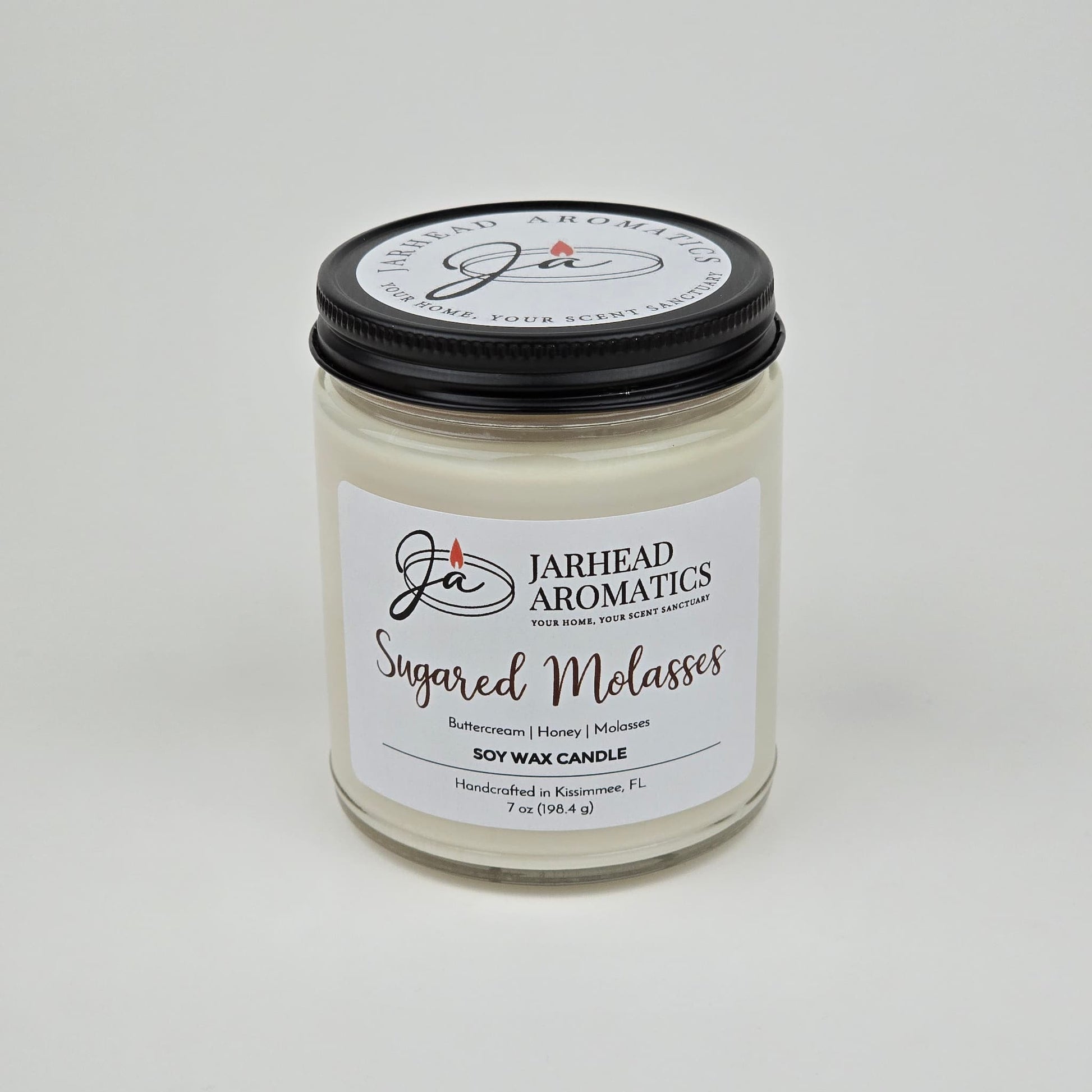 The Jarhead Aromatics Sugared Molasses Soy Wax Candle, labeled as "Sugared Molasses Soy Wax Candle | Brown Sugar, Honey, Cinnamon & Molasses Fall Candle," is a handmade soy candle that combines the warm, rich fragrance of brown sugar, honey, cinnamon, and molasses. Presented in a clear glass jar with a black lid and a crisp white label, this candle offers both an elegant look and an irresistible autumn-inspired aroma.