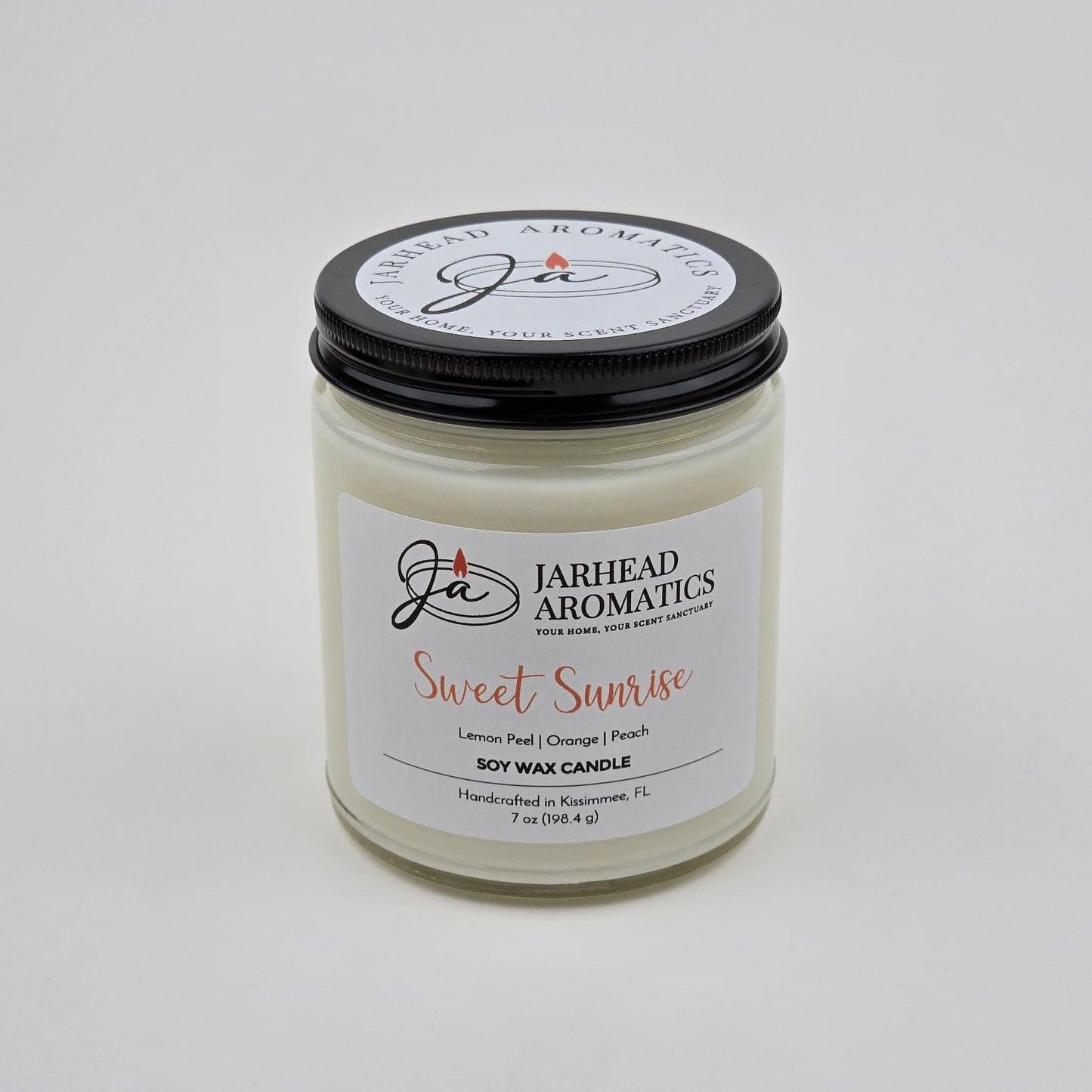 The Sweet Sunrise Soy Wax Candle by Jarhead Aromatics is a handcrafted citrus candle made in Kissimmee, FL. Presented in a clear glass jar with a black lid, this uplifting fragrance features bright notes of lemon peel, orange, agave, and peach—perfect for adding a burst of freshness to any space.