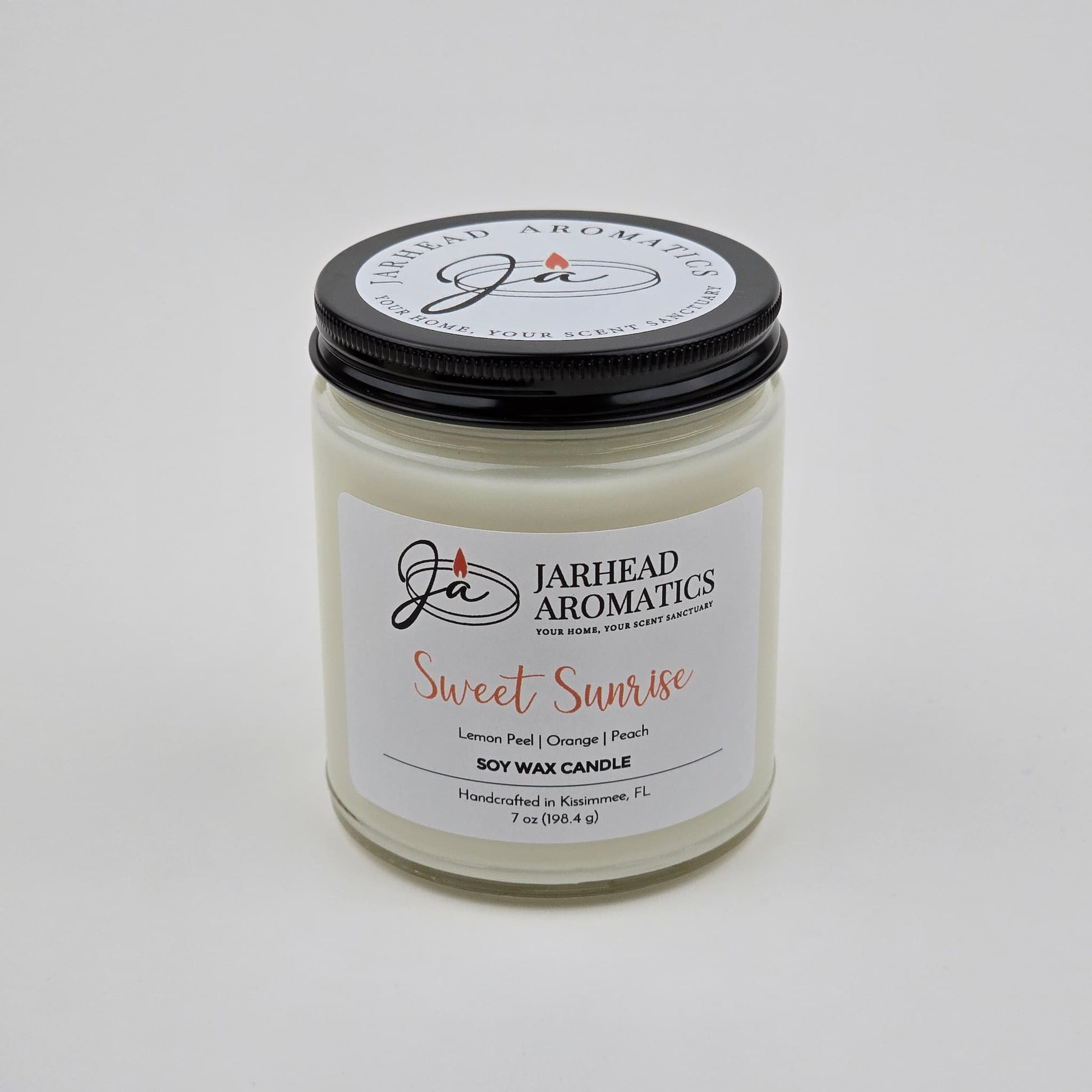 The Sweet Sunrise Soy Wax Candle by Jarhead Aromatics is a handcrafted citrus candle made in Kissimmee, FL. Presented in a clear glass jar with a black lid, this uplifting fragrance features bright notes of lemon peel, orange, agave, and peach—perfect for adding a burst of freshness to any space.