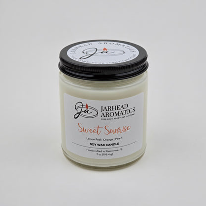 The Sweet Sunrise Soy Wax Candle by Jarhead Aromatics is a handcrafted citrus candle made in Kissimmee, FL. Presented in a clear glass jar with a black lid, this uplifting fragrance features bright notes of lemon peel, orange, agave, and peach—perfect for adding a burst of freshness to any space.