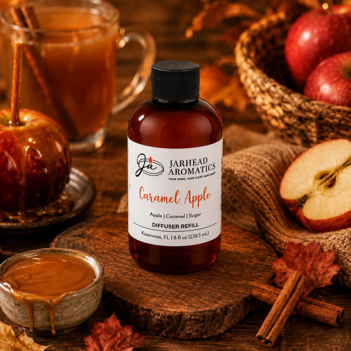 A bottle of Jarhead Aromatics Caramel Apple Diffuser Refill | Crisp Apple, Rich Caramel & Warm Spice sits on a rustic wooden table surrounded by fresh apples, gooey caramel, a classic caramel apple, a cozy mug, autumn leaves, and burlap—perfectly capturing the inviting essence of fall home fragrance.