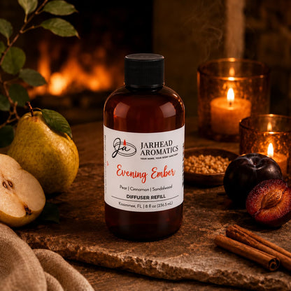 A bottle of Jarhead Aromatics Evening Ember Diffuser Refill | Plum, Sandalwood & Soft Smoke is set on a table alongside pears, plums, cinnamon sticks, and a glowing candle, all against a warm, rustic backdrop that creates a cozy and aromatic home fragrance ambiance.