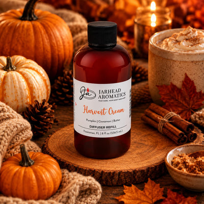 A bottle of Jarhead Aromatics Harvest Cream Diffuser Refill | Pumpkin Spice, Brown Sugar & Vanilla Cream rests among pumpkins, autumn leaves, a cup of whipped coffee, cinnamon sticks, and a glowing candle on a rustic wooden table—filling your home with the perfect cozy fall fragrance for an inviting autumn atmosphere.