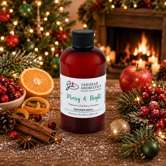 An amber plastic Merry & Bright Diffuser Refill by Jarhead Aromatics sits on a wooden surface surrounded by cranberries, orange slices, cinnamon sticks, pine branches, and Christmas ornaments in front of a fireplace.