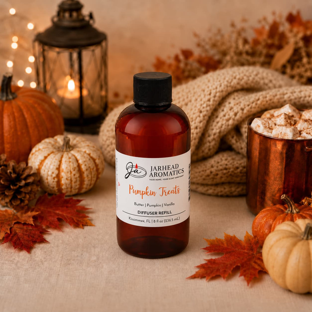A bottle of Jarhead Aromatics’ Pumpkin Treats Diffuser Refill | Pumpkin, Caramel & Maple Pecan rests on a beige cloth, surrounded by pumpkins, autumn leaves, a lantern, and warm decorative lights, creating a cozy fall atmosphere filled with the inviting fragrance of pumpkin spice, caramel, and maple pecan.