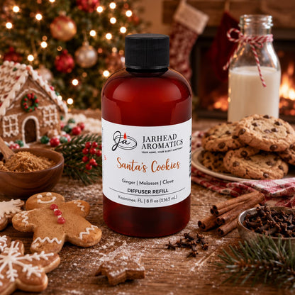 A bottle of Jarhead Aromatics Santa’s Cookies Diffuser Refill sits on a wooden table surrounded by a gingerbread man, chocolate chip cookies, cinnamon sticks, and a glass of milk in front of a fireplace.