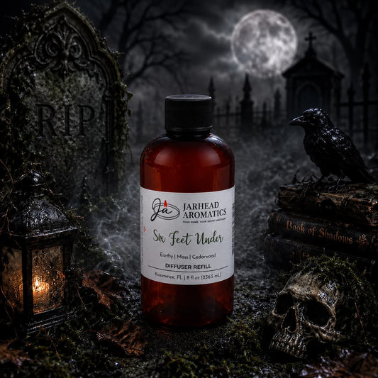 A bottle of Jarhead Aromatics’ Six Feet Under Diffuser Refill | Damp Earth, Moss & Ancient Oak rests atop a stone surrounded by a skull, crow, lantern, and Book of Shadows; its earthy aroma weaves through the moonlit cemetery adorned with gravestones and framed by a wrought iron gate, setting an unforgettable home fragrance mood.