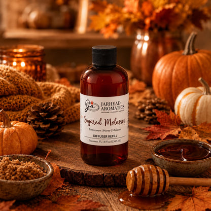 A bottle of Jarhead Aromatics Sugared Molasses Diffuser Refill | Buttercream, Honey & Dark Molasses rests on a wooden table, surrounded by pumpkins, leaves, honey, brown sugar, and autumn decor—a perfect way to fill your home with a cozy seasonal fragrance.