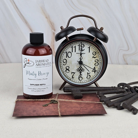 A Jarhead Aromatics Minty Breeze - Diffuser Refill sits next to a vintage black alarm clock, three antique keys, and a brown envelope on a light background.