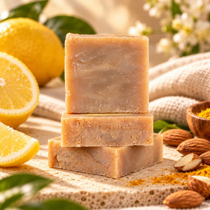 A stack of three beige Almond + Lemon Natural Handmade Soap | Turmeric & Shea Butter Bar Soap, surrounded by lemon slices, almonds, and turmeric powder.