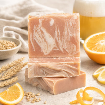 Three bars of Jarhead Aromatics Belgium Wheat + Citrus Handmade Craft Beer Artisan Soap are stacked on a table, surrounded by orange slices, wheat, and a glass of frothy beer in the background—highlighting the soap’s natural ingredients and bright citrus and wheat beer scent.