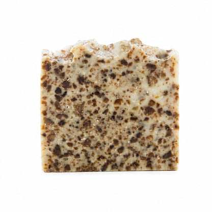 A rectangular bar of Jarhead Aromatics’ Black Soap + Lavender Handmade Natural Artisan Soap, featuring a rough, uneven top edge and a speckled brown and cream pattern throughout, stands upright against a white background.
