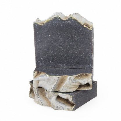 A handcrafted soap by Jarhead Aromatics, the Charcoal + Tonka Handmade Artisan Soap features pages sculpted to resemble an open book, with textured stone-like surfaces, rough and uneven edges, and a marbled blend of dark gray and light hues reminiscent of activated charcoal.