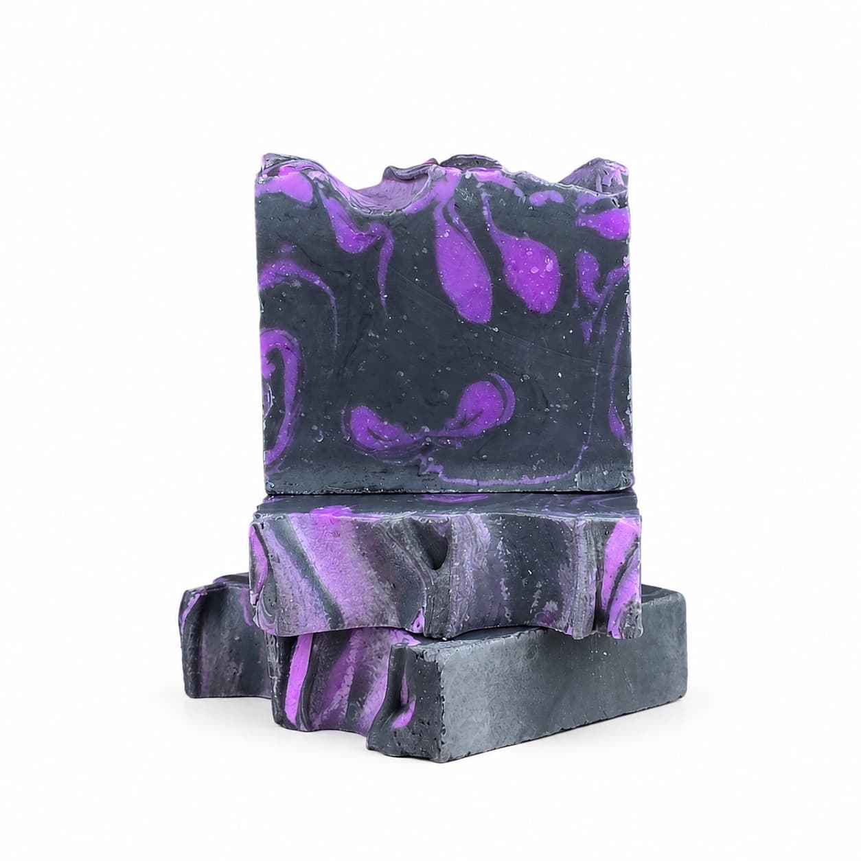Three rectangular bars of Jarhead Aromatics’ Citrus + Sandalwood Handmade Coconut Milk Artisan Soap, featuring a marbled black and purple design, are stacked on a white background. The top bar stands upright, highlighting its wavy pattern and uneven top edge.
