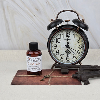 A vintage alarm clock, old keys, and a brown envelope sit beside Jarhead Aromatics’ Coastal Timber Diffuser Refill, filling the space with the spa-inspired scent of teakwood, leather, and amber against a marble backdrop.