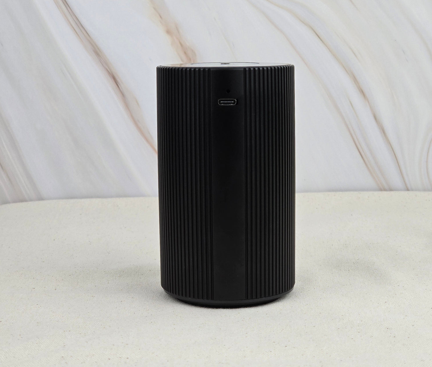 The Jarhead Aromatics Cold Air Diffuser - Portable & Rechargeable features a black cylindrical design with vertical grooves, a charging port near the top, and an earthy look—perfect for diffusing essential oils anywhere.