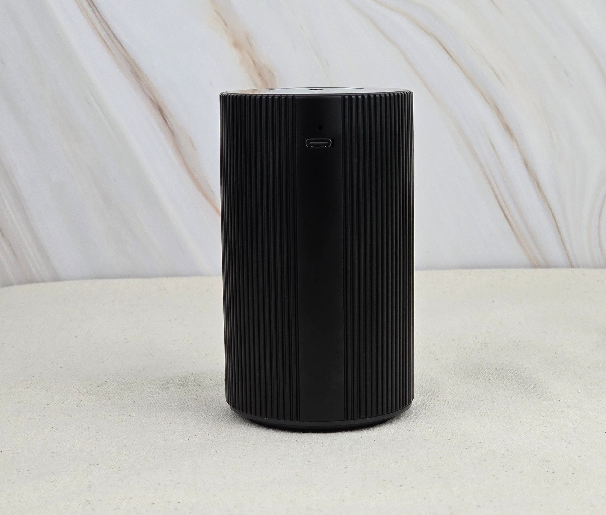 The Jarhead Aromatics Cold Air Diffuser - Portable & Rechargeable features a black cylindrical design with vertical grooves, a charging port near the top, and an earthy look—perfect for diffusing essential oils anywhere.