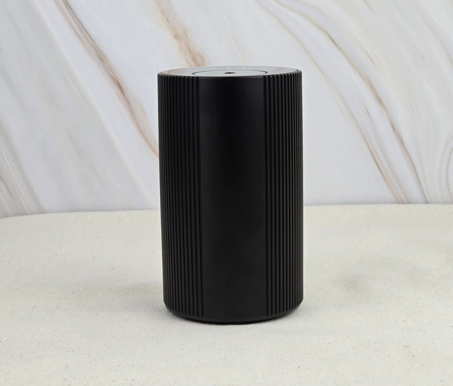 The Jarhead Aromatics Cold Air Diffuser – Portable & Rechargeable stands sleek and black with vertical grooves on a light, textured surface, set against a marble-patterned background for an earthy, calming vibe.