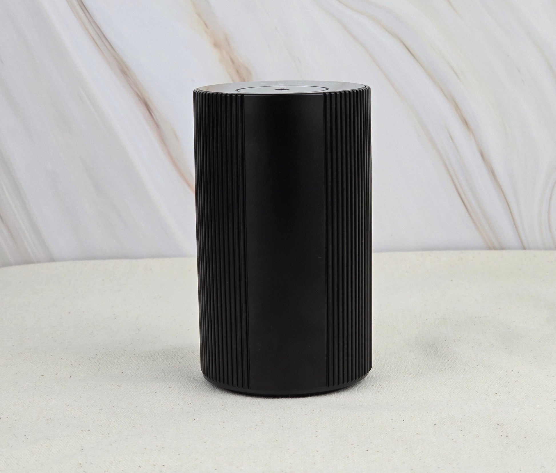 The Jarhead Aromatics Cold Air Diffuser – Portable & Rechargeable stands sleek and black with vertical grooves on a light, textured surface, set against a marble-patterned background for an earthy, calming vibe.
