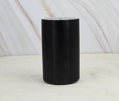 The Jarhead Aromatics Cold Air Diffuser – Portable & Rechargeable stands sleek and black with vertical grooves on a light, textured surface, set against a marble-patterned background for an earthy, calming vibe.