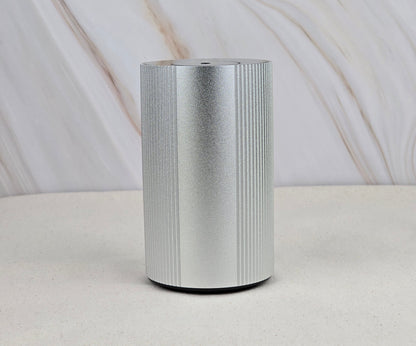 The Jarhead Aromatics Cold Air Diffuser - Portable & Rechargeable features a sleek silver cylindrical design with vertical ridges, displayed on a light surface and beige backdrop, evoking an earthy, woodsy ambiance inspired by essential oils.