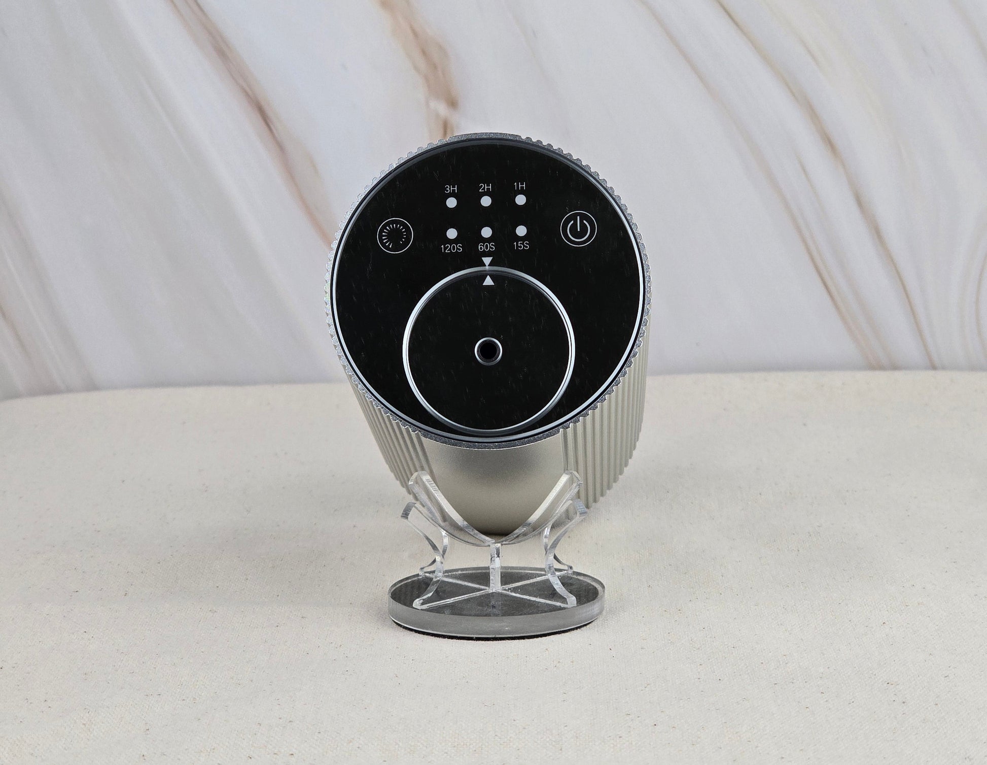 The Jarhead Aromatics Cold Air Diffuser – Portable & Rechargeable – features a sleek cylindrical design with a black control panel and buttons, displayed on a minimalist silver stand against a light marbled background for an earthy, elegant look.